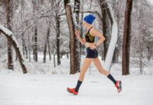 Jogging in any weather. Young hot runner woman running in winter park in snow weather